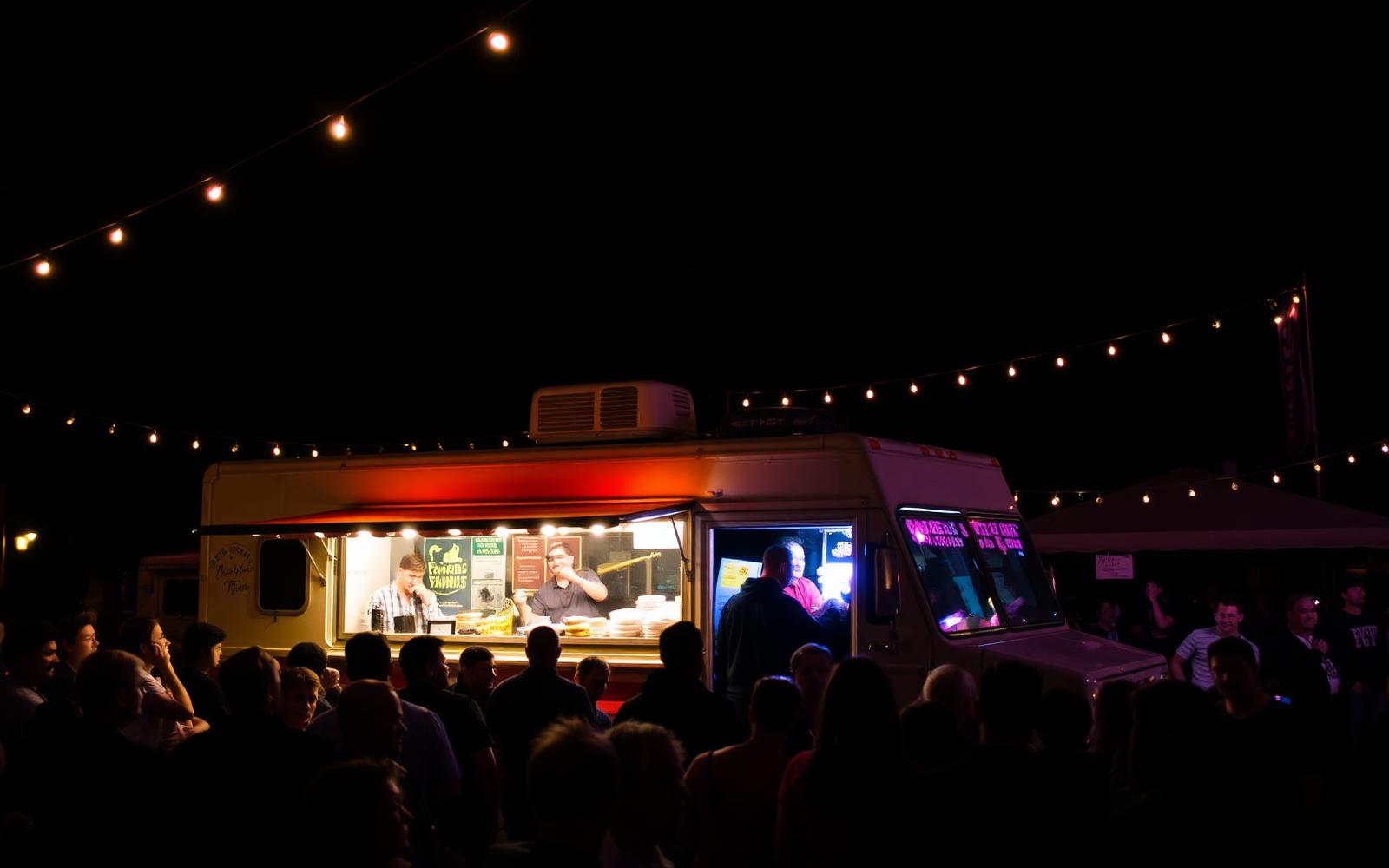 Food truck lit up at night with a crowd